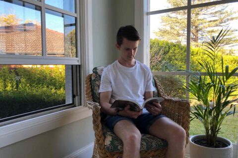 Man reading a book in his home in Sydney as the most powerful Whole House Fan in Australia cools him being the green choice